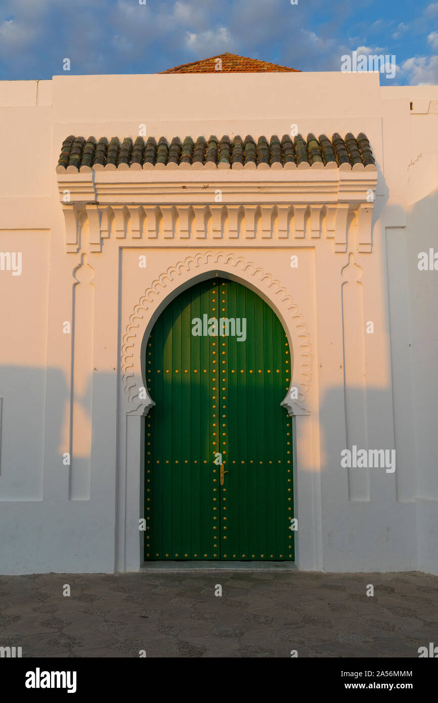 Porte en bois peint en vert avec une décoration aux couleurs de l'or dans la médina d'Asilah, Maroc au soleil couchant Banque D'Images