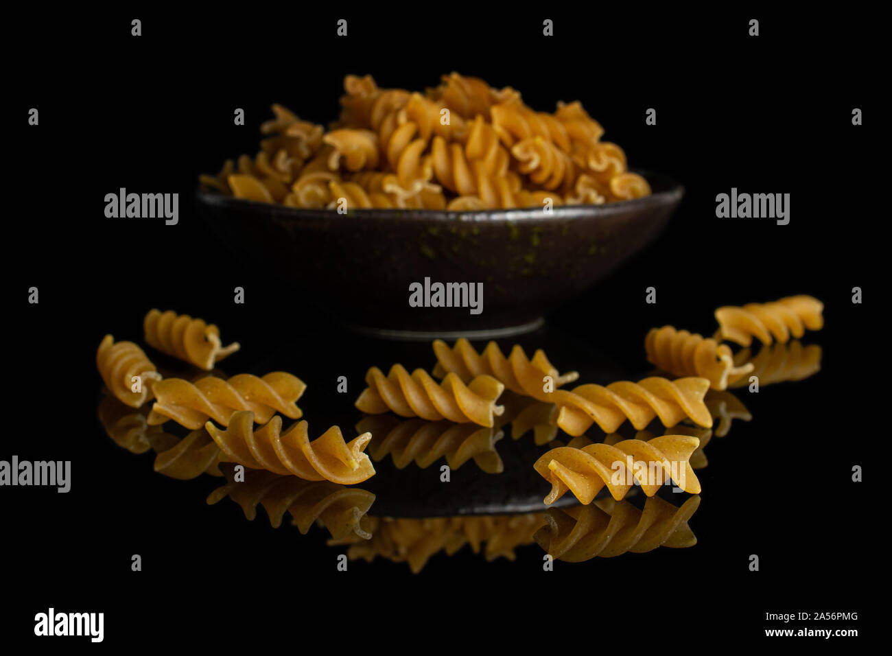 Beaucoup d'aliments complets secs fusilli dans dark brown Bol en céramique isolé sur verre noir Banque D'Images