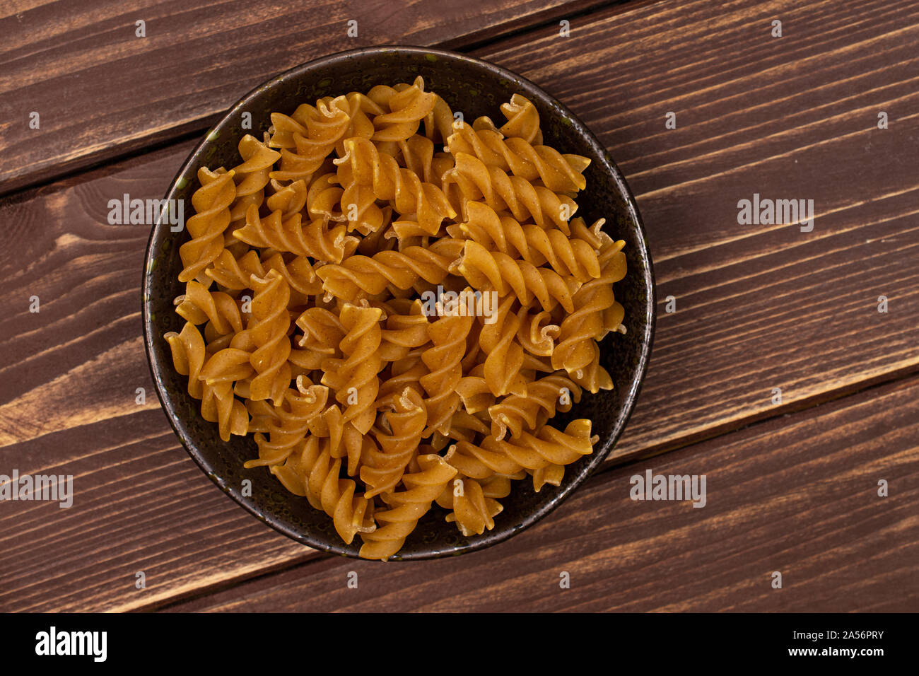 Beaucoup d'aliments complets secs fusilli dans dark brown Bol en céramique flatlay sur bois marron foncé Banque D'Images