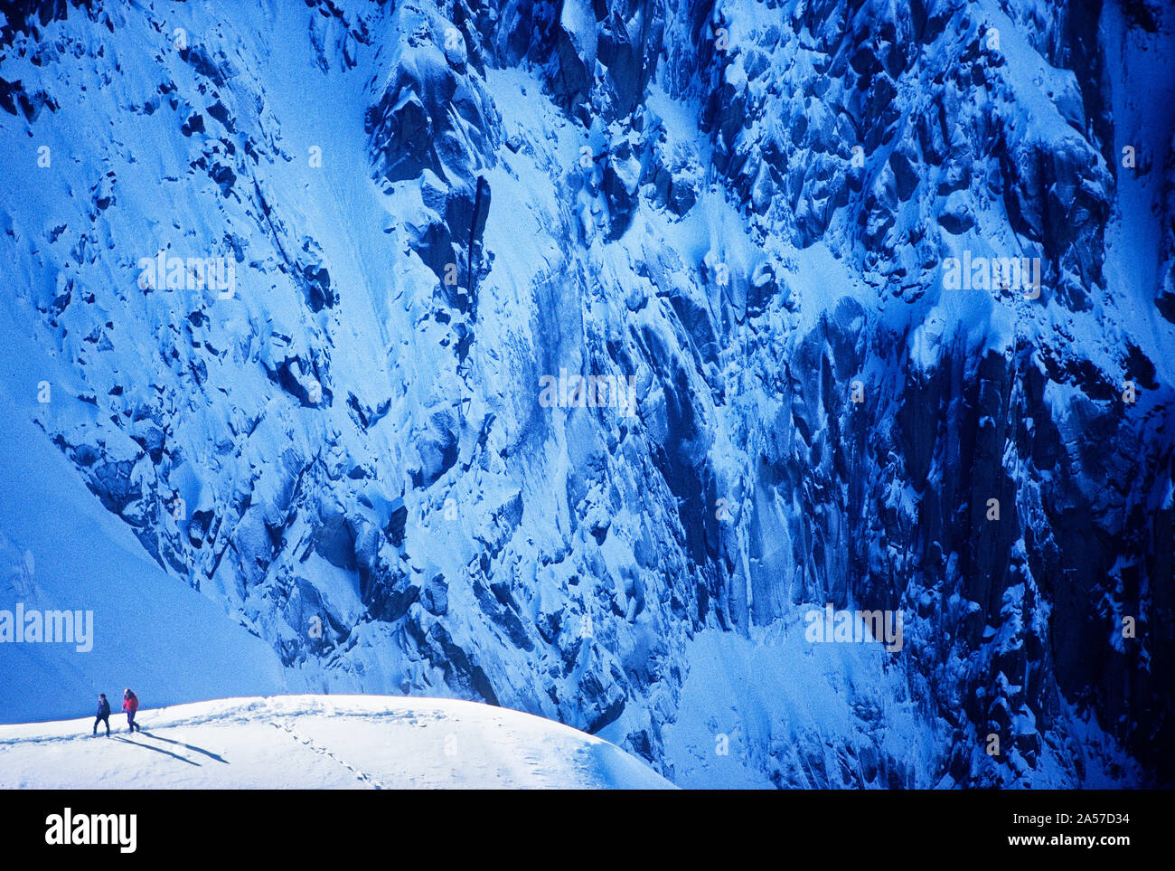 Deux alpinistes sur une arête de neige avec la face Ouest de l'Aiguille de Plan au-delà de la France, les Aiguilles de Chamonix Banque D'Images