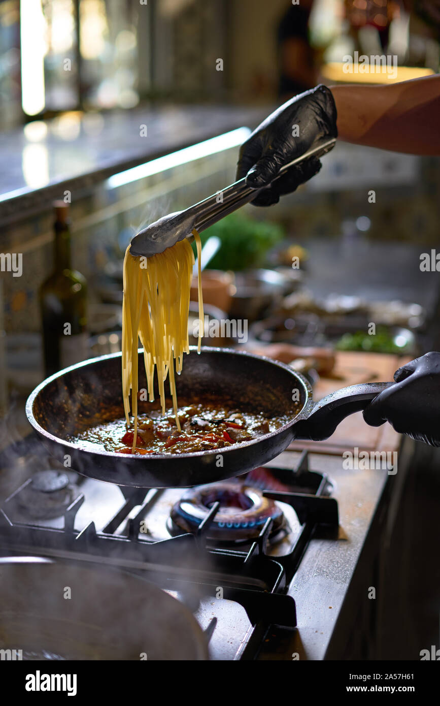 Concept alimentaire. Le chef ajoute fry spaghetti dans une casserole les tomates et les huîtres. Le processus de cuisson de spaghettis aux fruits de mer. Banque D'Images