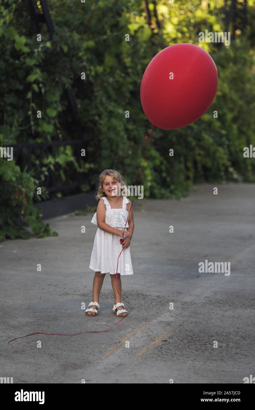 Happy young girl in white sundress holding immense ballon rouge Banque D'Images