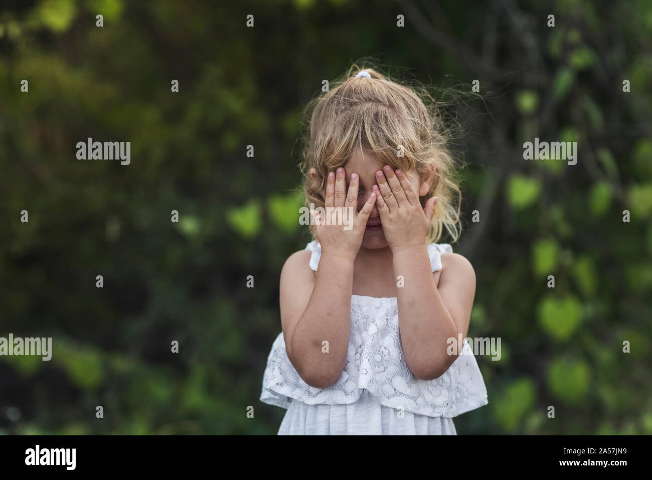 Jeune fille en robe d'été couvrant le visage avec les mains potelées Banque D'Images