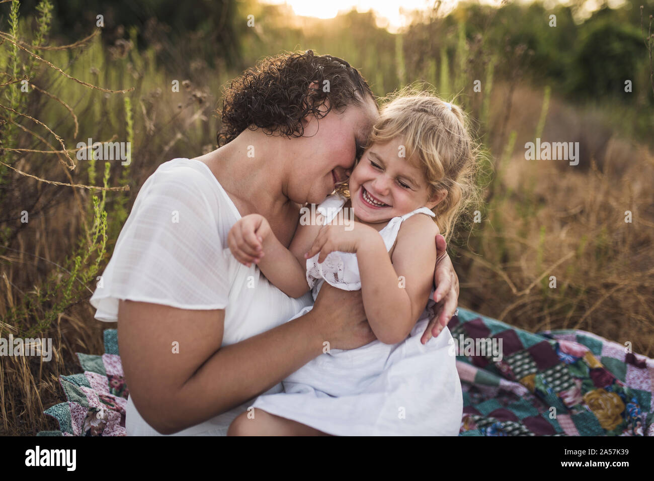 Chatouilles maman sourire rire 4 ans fille sur la courtepointe dans de grandes plantes Banque D'Images