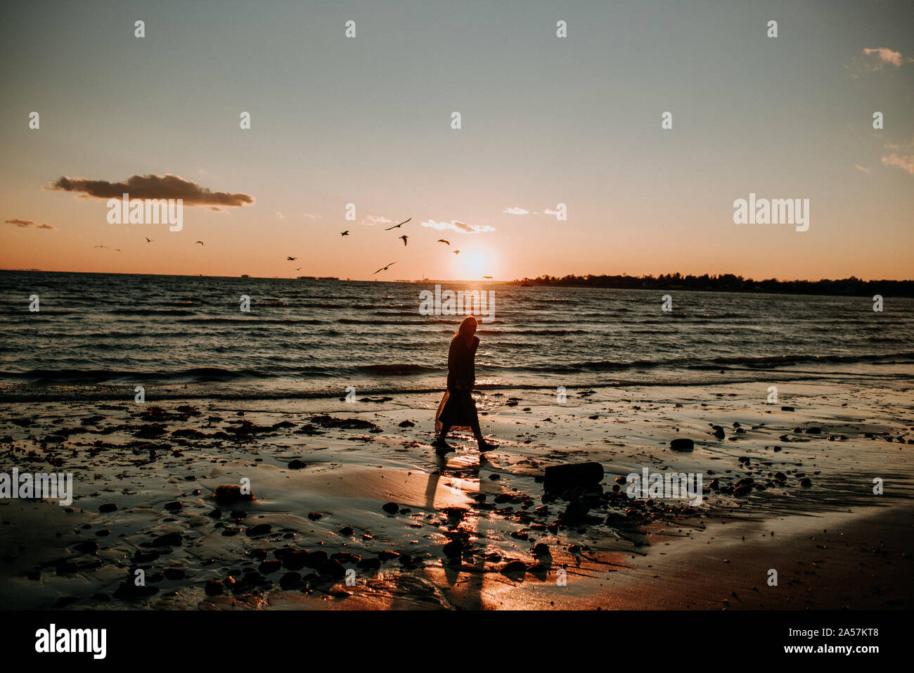 Femme marche sur la plage au coucher du soleil Banque D'Images