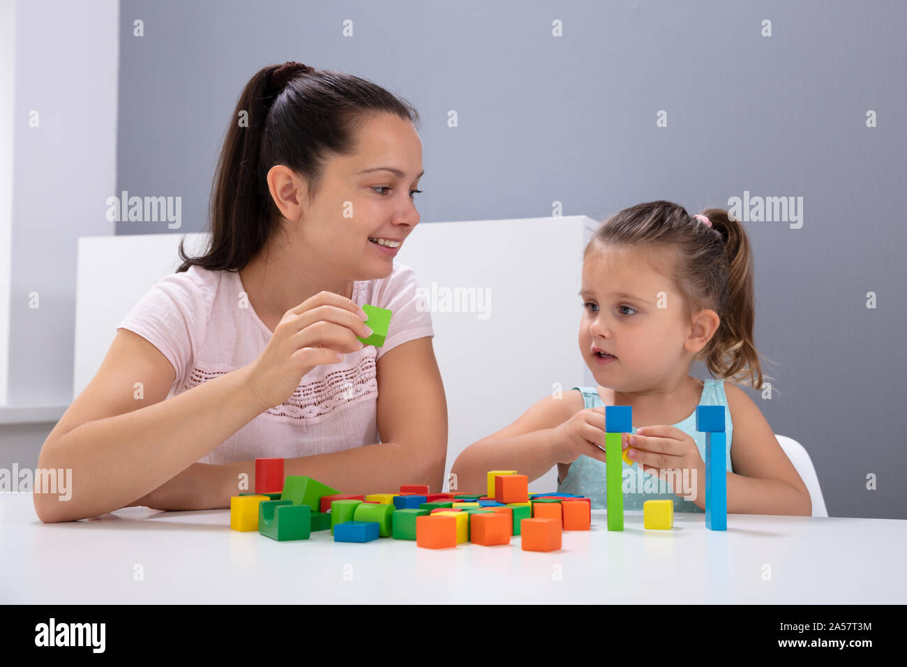 Smiling travailleuse en garderie enfant jouant avec des blocs d'Empilage sur blanc 24 Banque D'Images