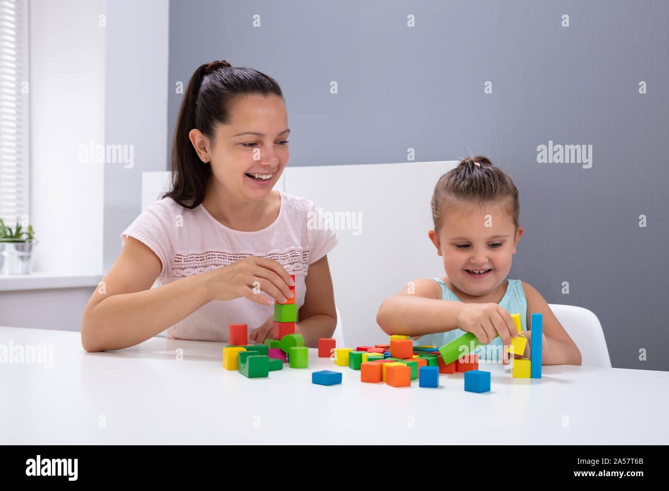 Smiling travailleuse en garderie enfant jouant avec des blocs d'Empilage sur blanc 24 Banque D'Images