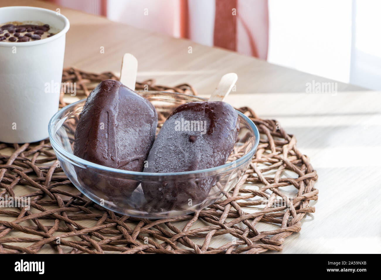 Végétalien premières glaces faites maison, fait à partir de la banane et la crème de coco, couverts de chocolat naturel. Petite partie dans du papier blanc tasse et deux sucettes glacées Banque D'Images