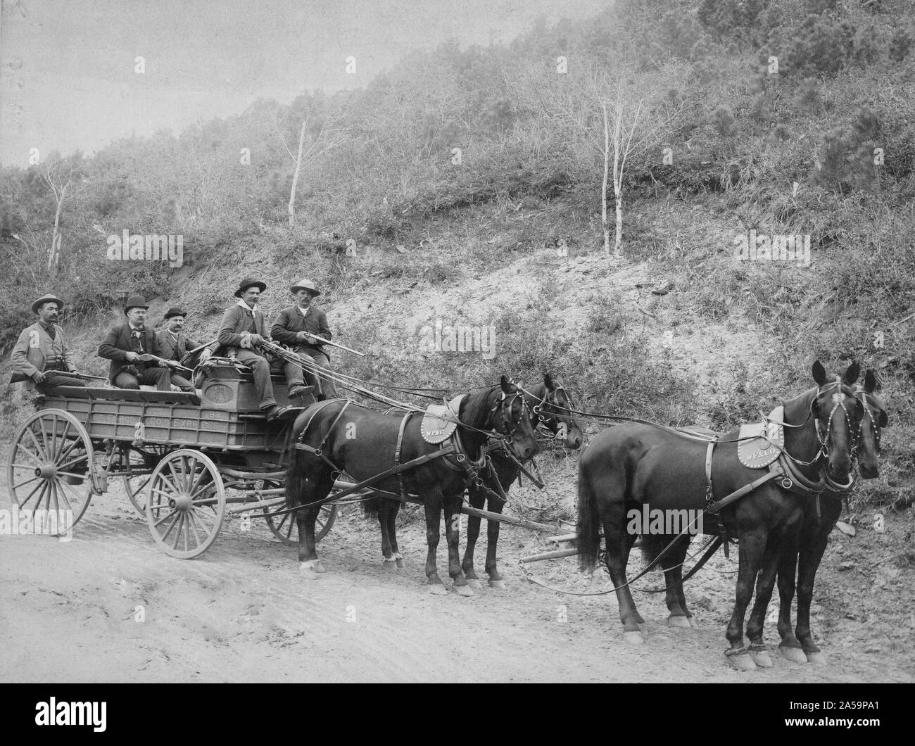 Cinq hommes, tenant des fusils, en wagon découvert, sur une route de campagne. Banque D'Images