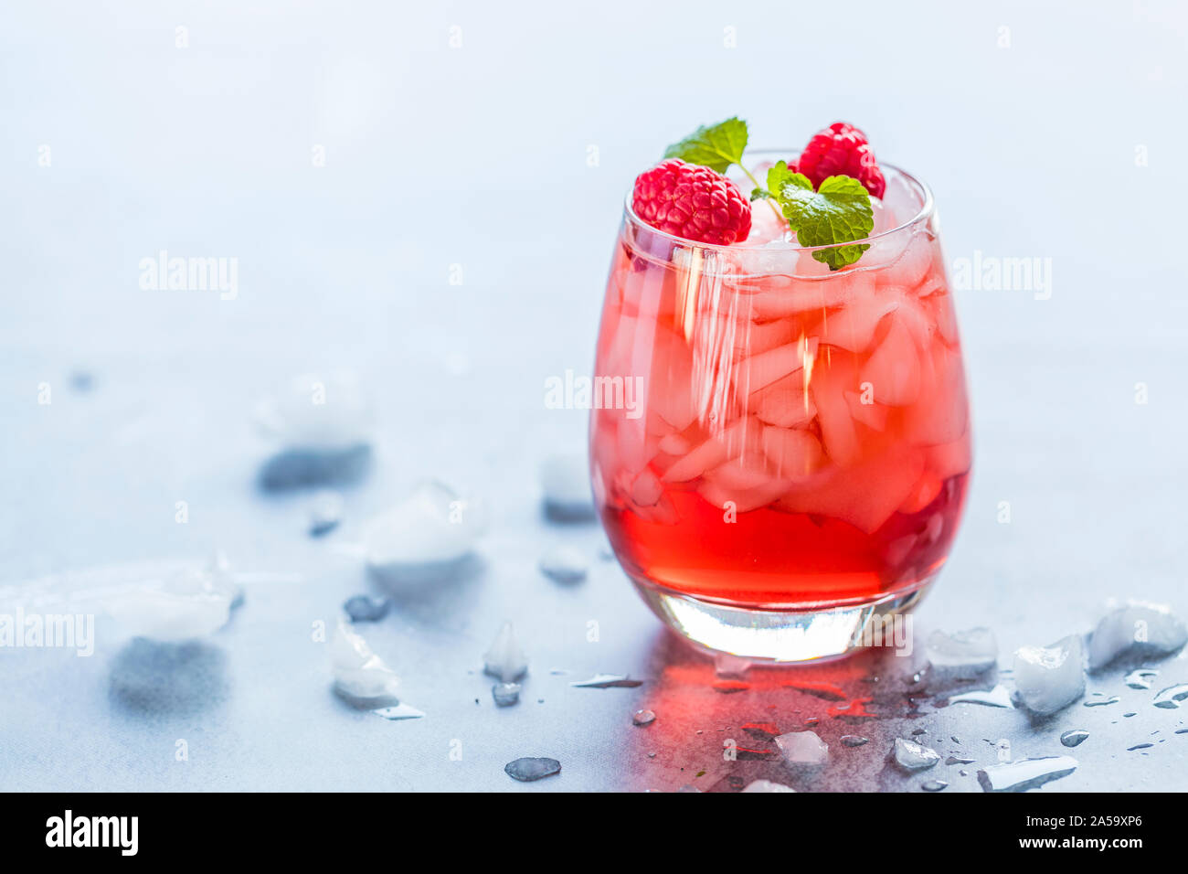 Close-up of a une rafraîchissante boisson translucide rouge avec de la glace et les framboises. Le jus est garnie d'une feuille verte, et therer sont des morceaux de glace et Banque D'Images