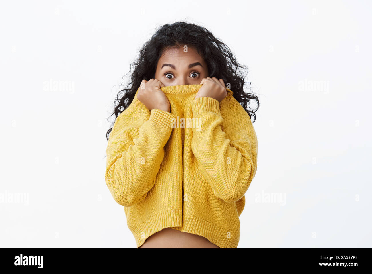 Surpris et effrayé cute young african american female student se cacher face à collier chandail, élargir les yeux d'une embuscade et se demande, lever les sourcils Banque D'Images