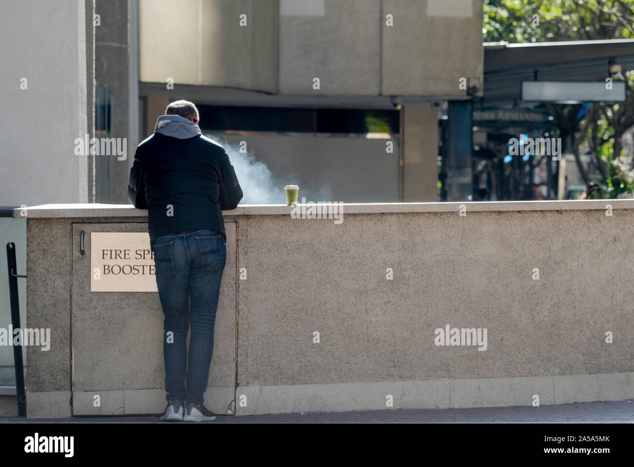 Un homme blanc d'âge moyen à l'opposé de l'appareil photo de fumer et boire du café à l'extérieur d'un seul bâtiment de ville de Sydney, Australie Banque D'Images