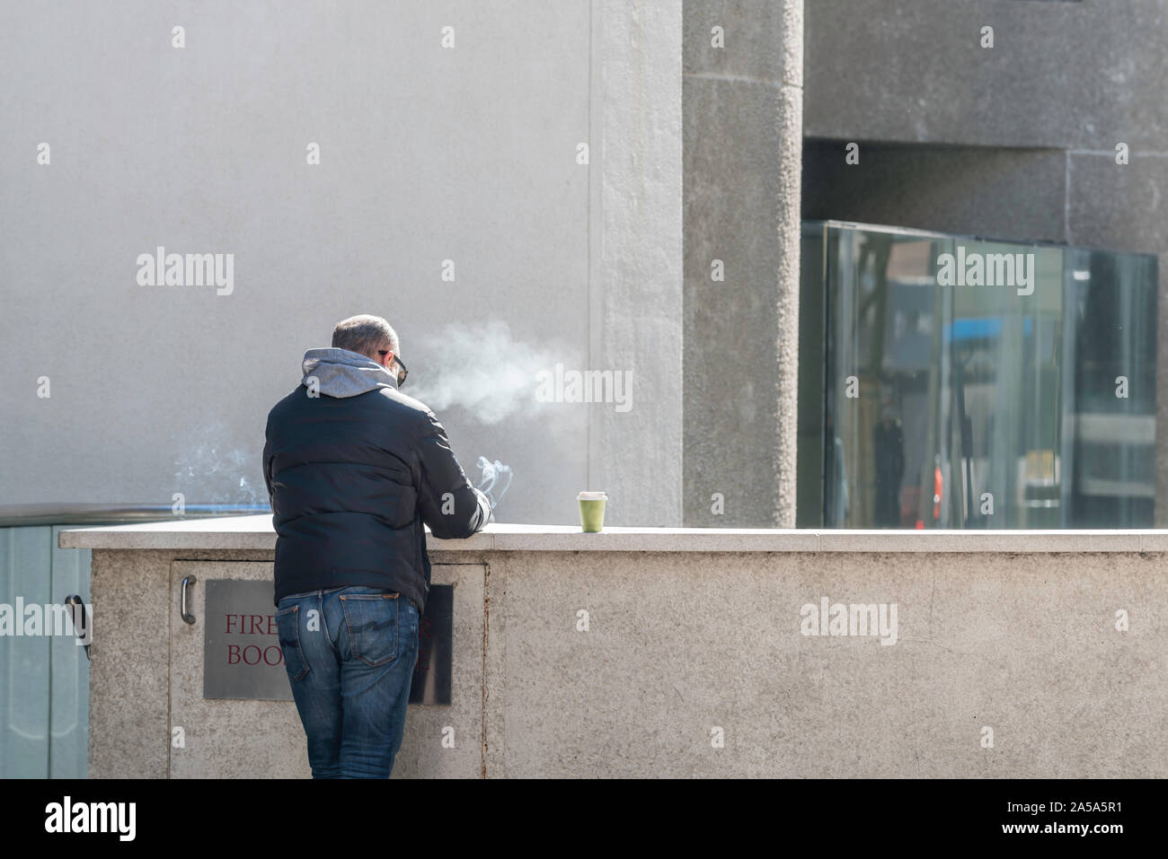 Un homme blanc d'âge moyen à l'opposé de l'appareil photo de fumer et boire du café à l'extérieur d'un seul bâtiment de ville de Sydney, Australie Banque D'Images