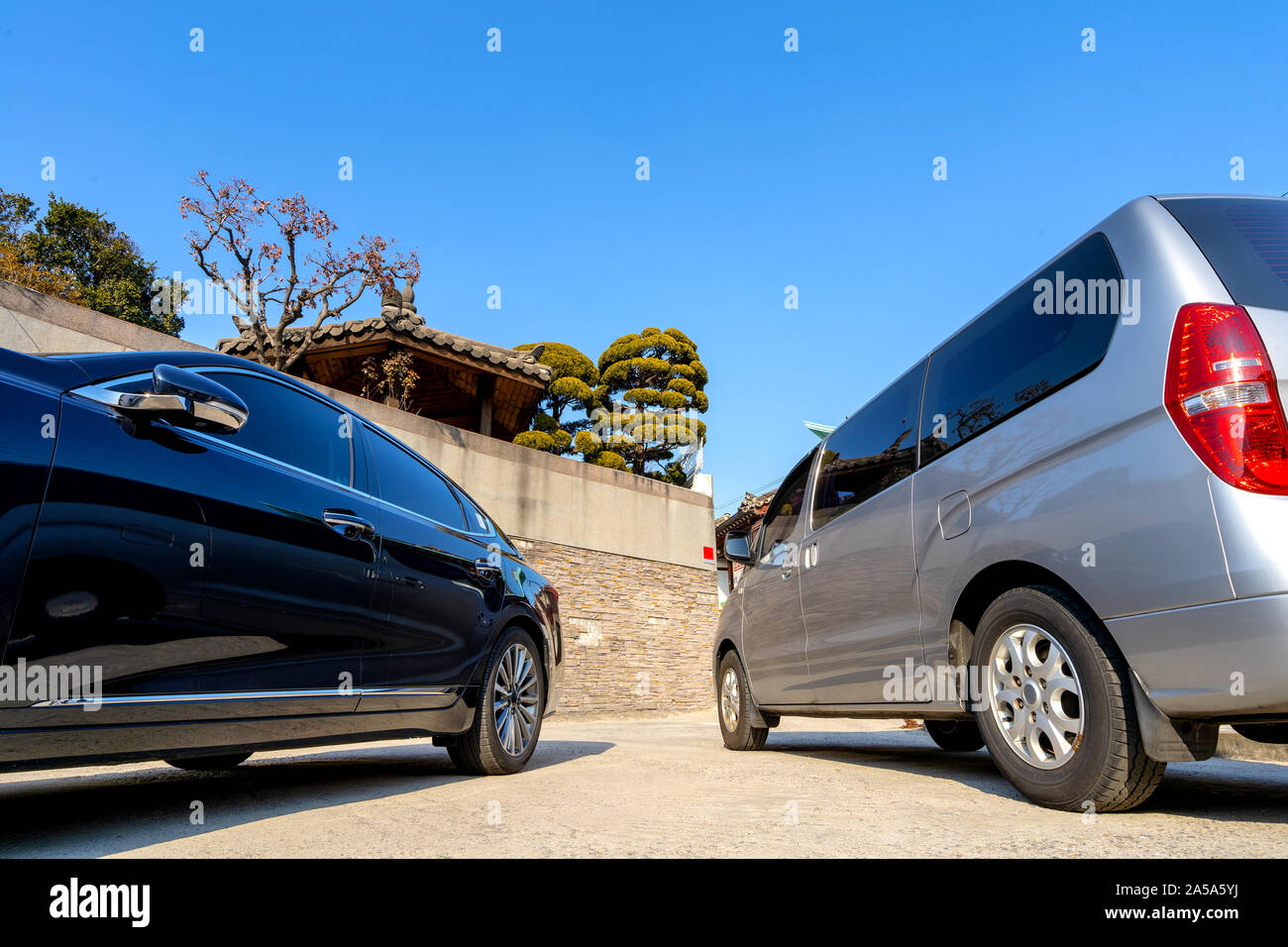 Voir entre deux voitures sur un parking en face d'un mur avec un peu de Coran jardin au-dessus d'elle. Banque D'Images