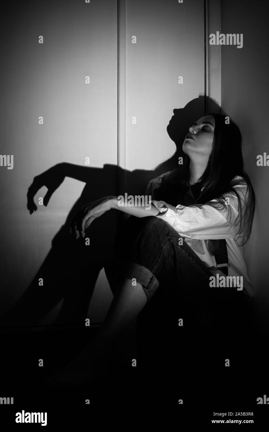 Triste jeune femme assise dans le coin sombre en regardant vers le haut, monochrome Banque D'Images