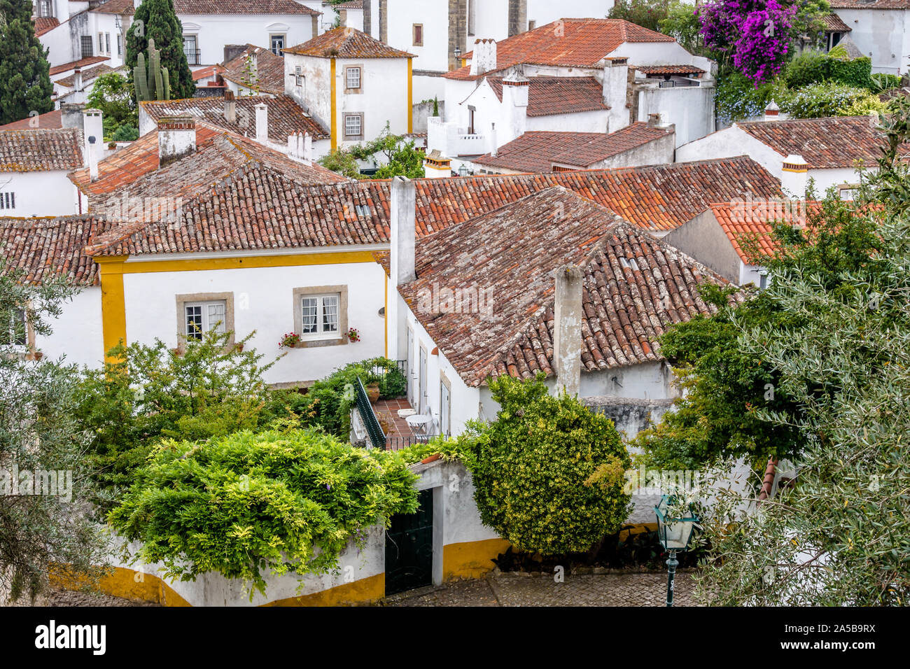 Vue plongeante sur la météo porté tuiles de maisons blanchies à la chaux et de jardins urbains à Obidos, ville historique du Portugal. Banque D'Images