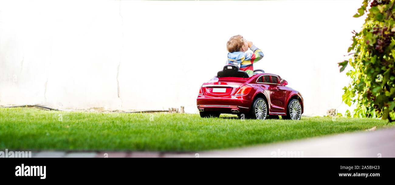 Petit garçon est au volant de sa petite voiture electro sur l'arrière-cour de la maison de ses parents, l'action qui fait que chaque petit garçon vraiment heureux Banque D'Images