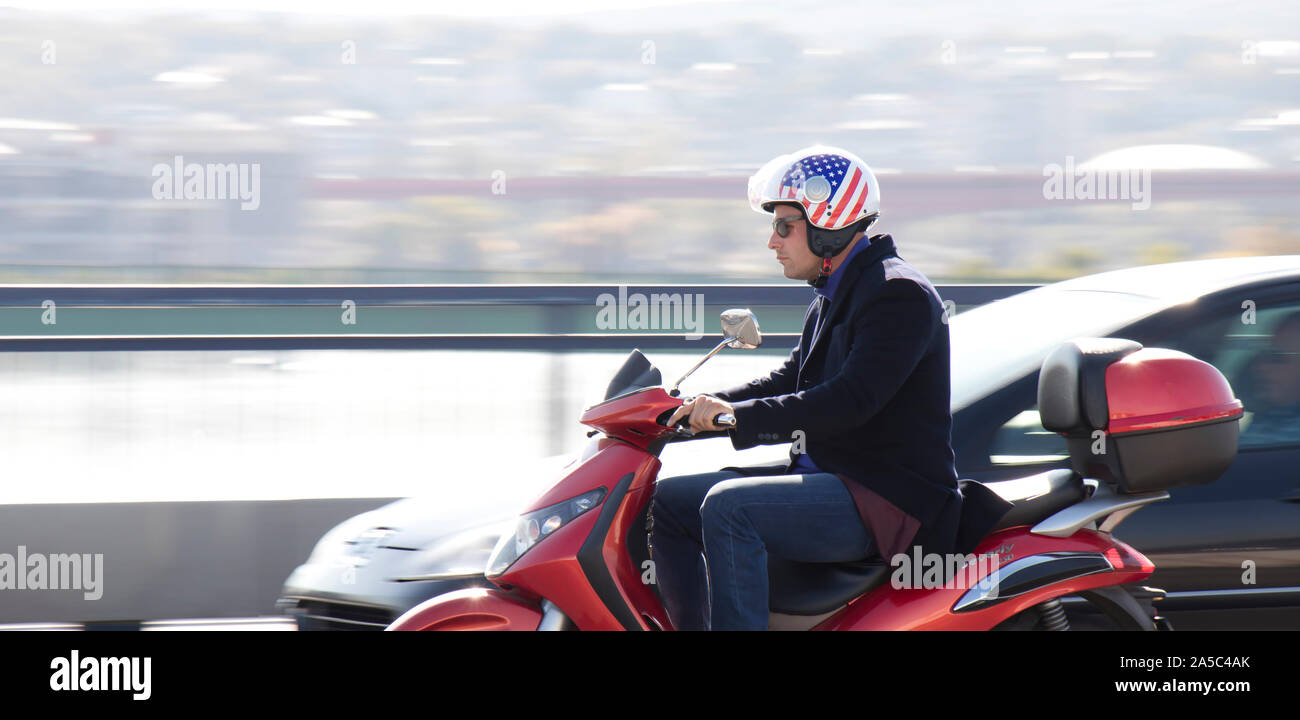 Belgrade, Serbie - 16 octobre 2019 : Un homme en portant des jeans et blazer drapeau américain équitation casque scooter rouge sur la ville street bridge dans l'état occupé Banque D'Images