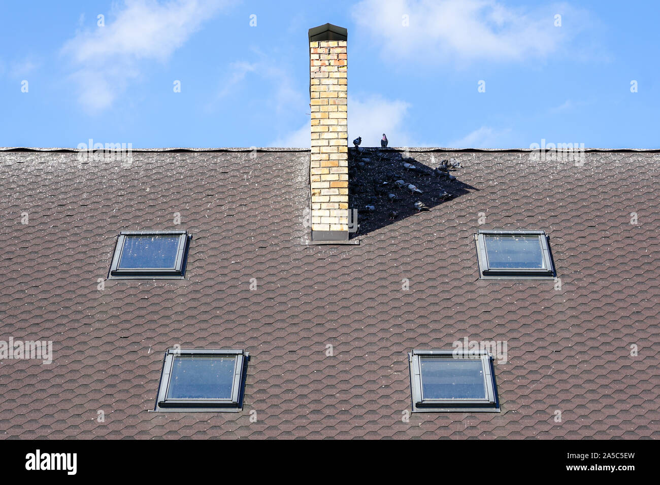 Toit de maison avec quatre fenêtres et cheminée, composition symétrique contre un ciel bleu Banque D'Images