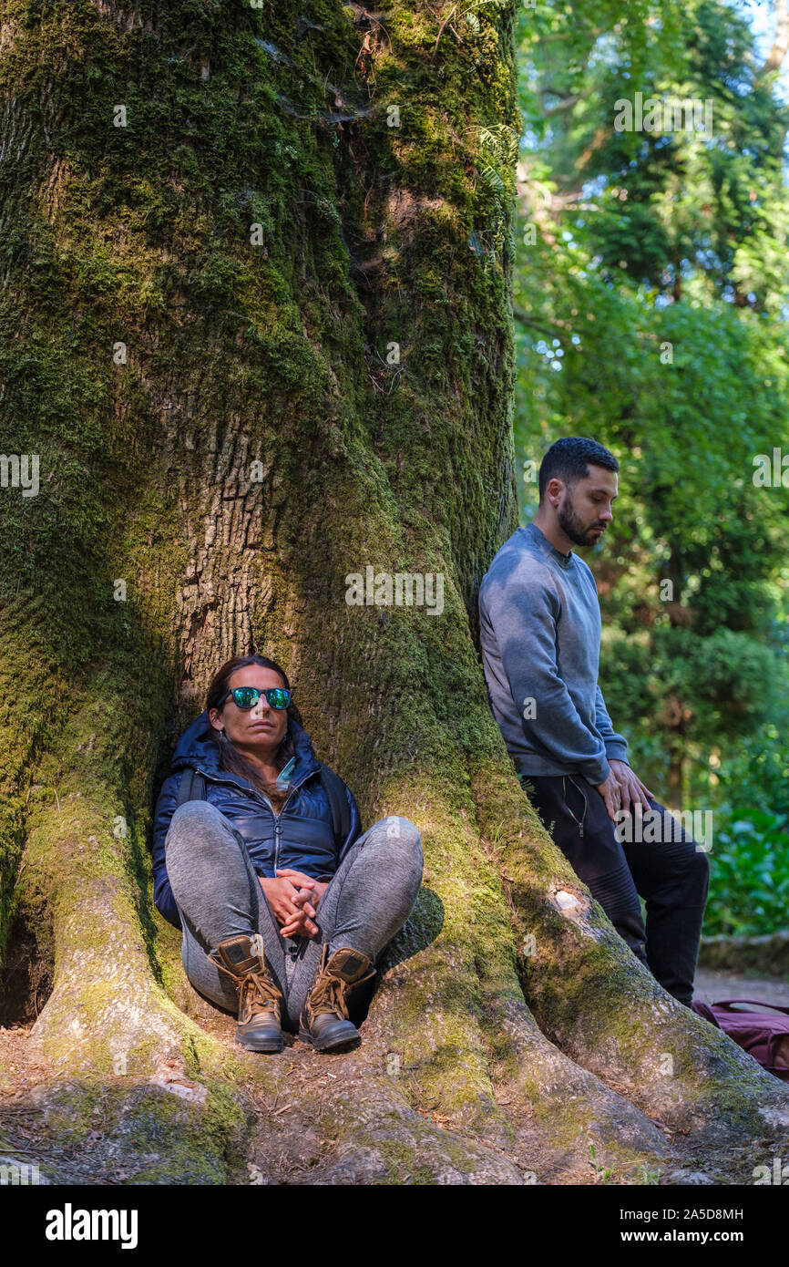 L'homme et la femme s'appuyant sur un arbre, les yeux fermés au cours d'une séance de bain forêt Banque D'Images