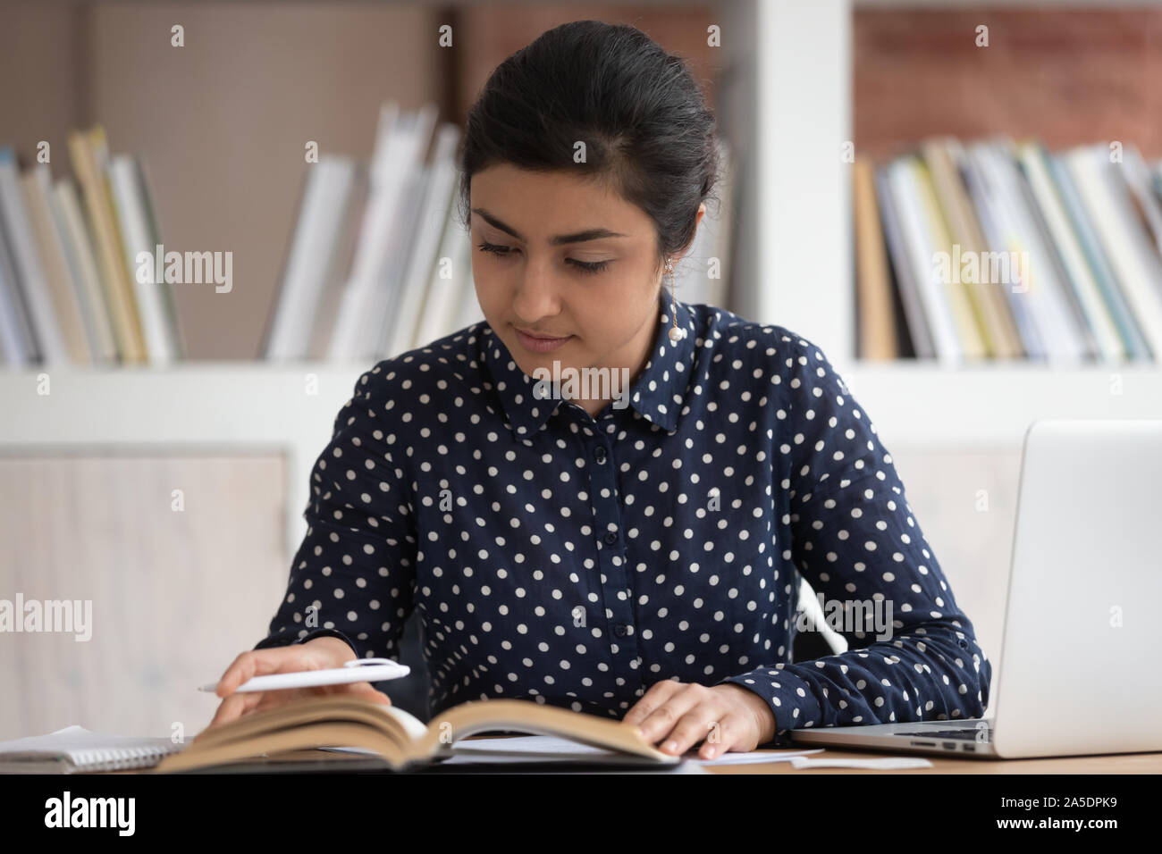 Indian Student sitting at desk tournez les pages Recherche information Banque D'Images