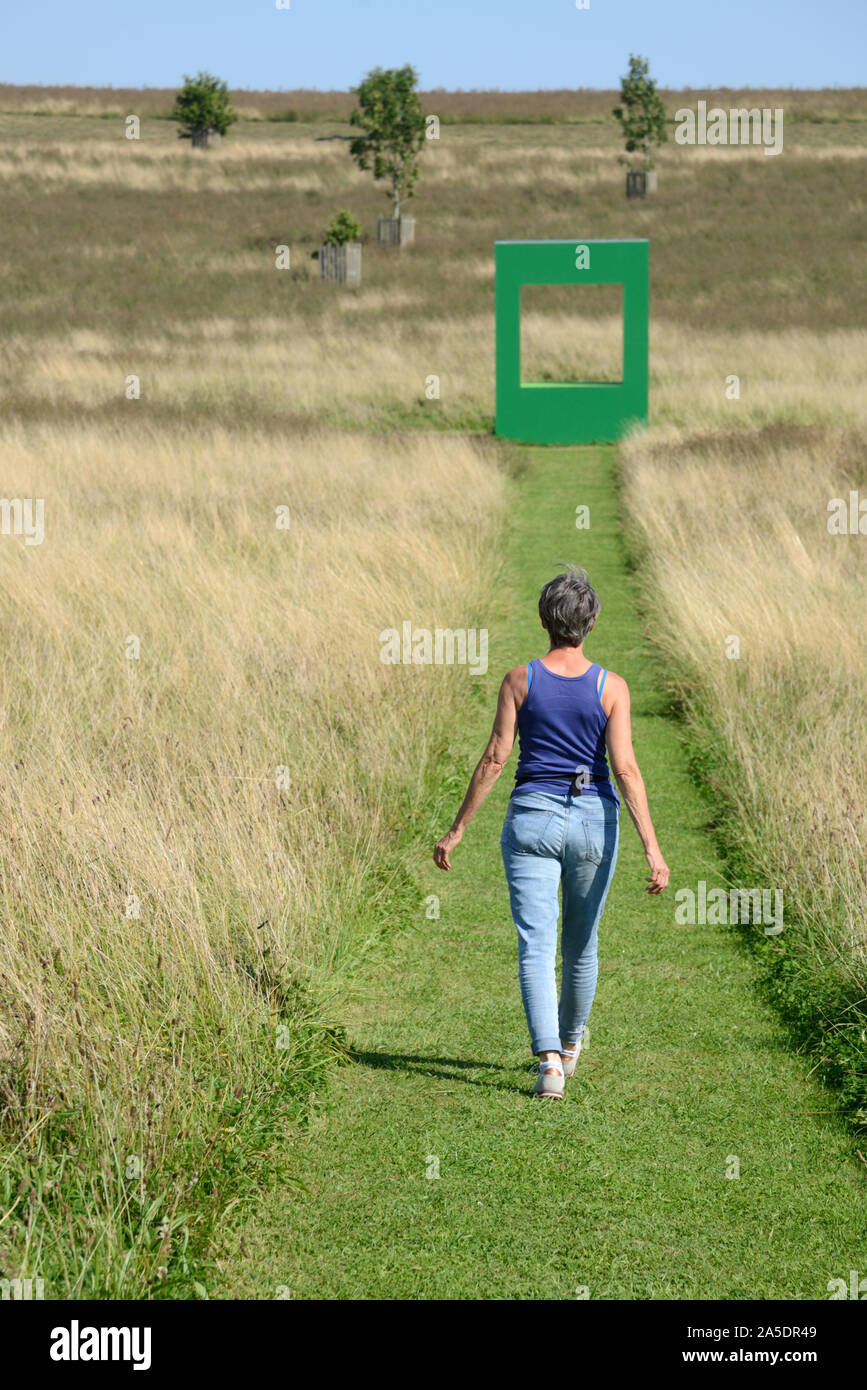 Femme européenne à marcher le long de l'herbe tondue en champ avec Logement Vert Art Installation par Krijn de Koning 2019 en arrière-plan Compton Verney Angleterre Banque D'Images