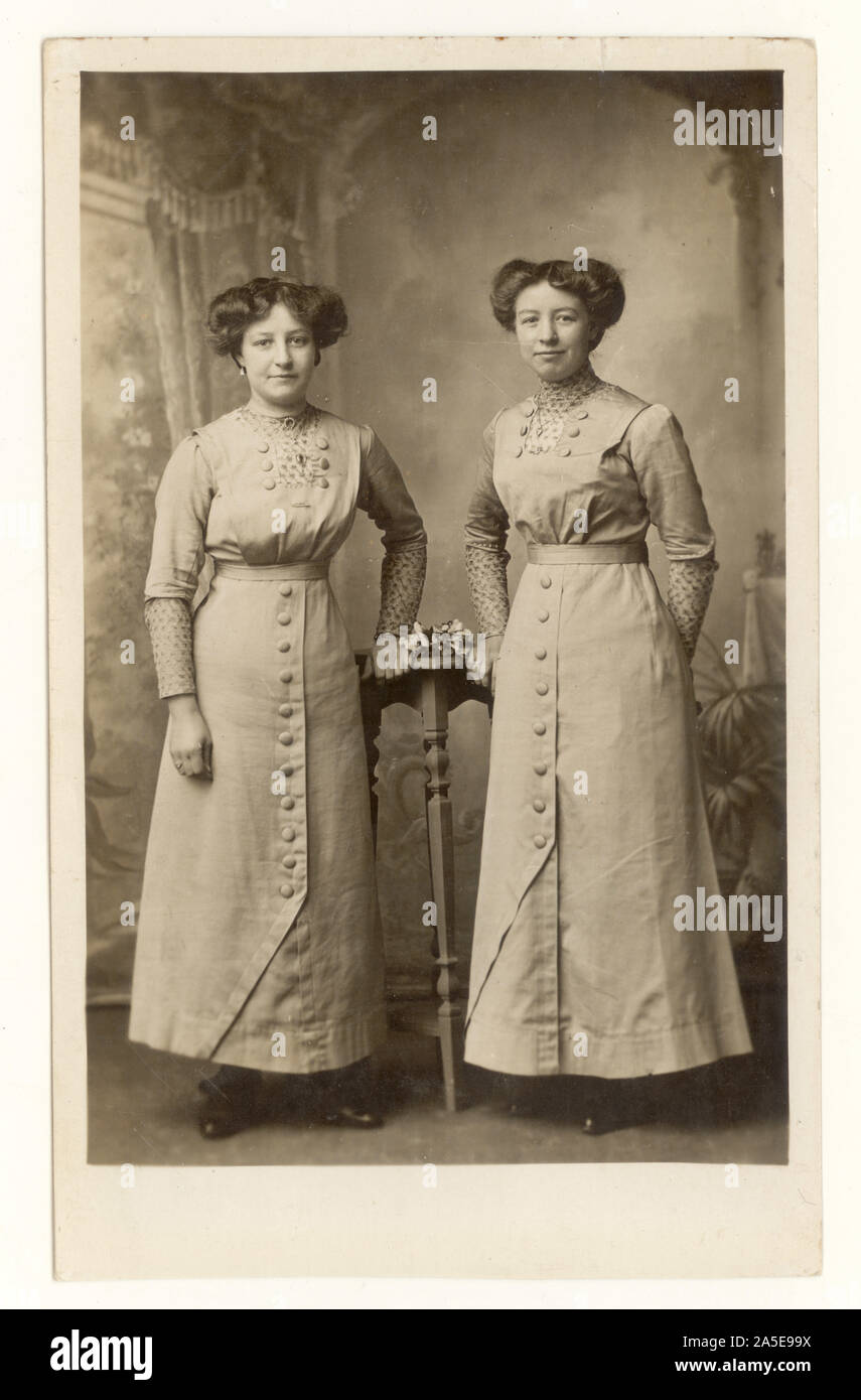 Original, clair début des années 1900 WW1 carte postale de jeunes femmes attirantes, sœurs, comme des jumeaux - frères et sœurs portant des robes de duvet à boutons assortis, chemisiers, longue hemline, petites femmes. Des coiffures intéressantes, des cheveux se sont emparés sur les côtés. Daté du 6 1914 juillet au dos, une photographie poignante prise plusieurs jours avant le déclenchement de la première guerre mondiale, au Royaume-Uni Banque D'Images