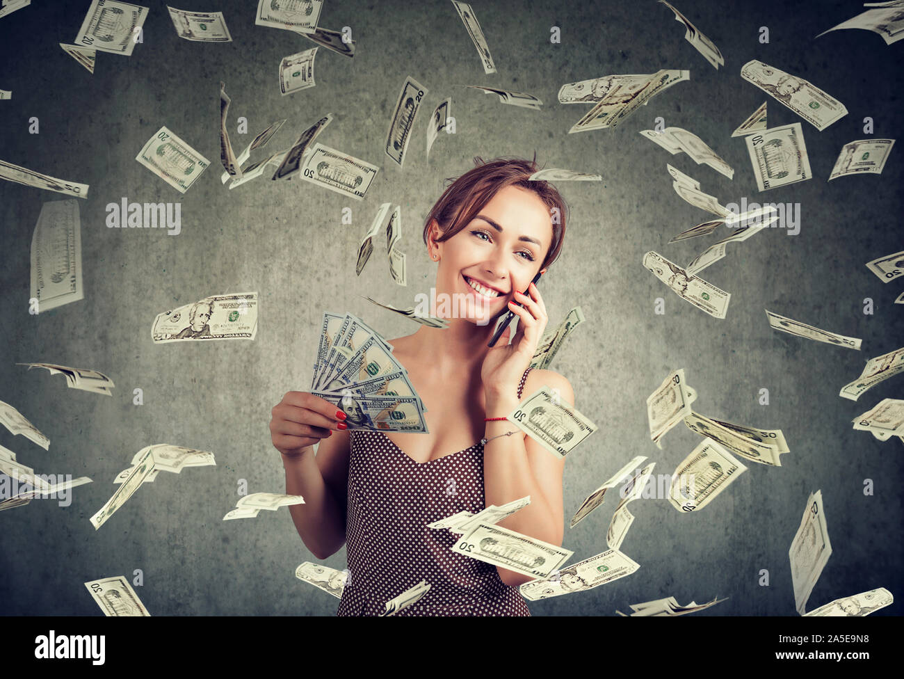 Jolie femme excité de parler sur un smartphone de la détention de monnaie, cashback dans dollar rain Banque D'Images