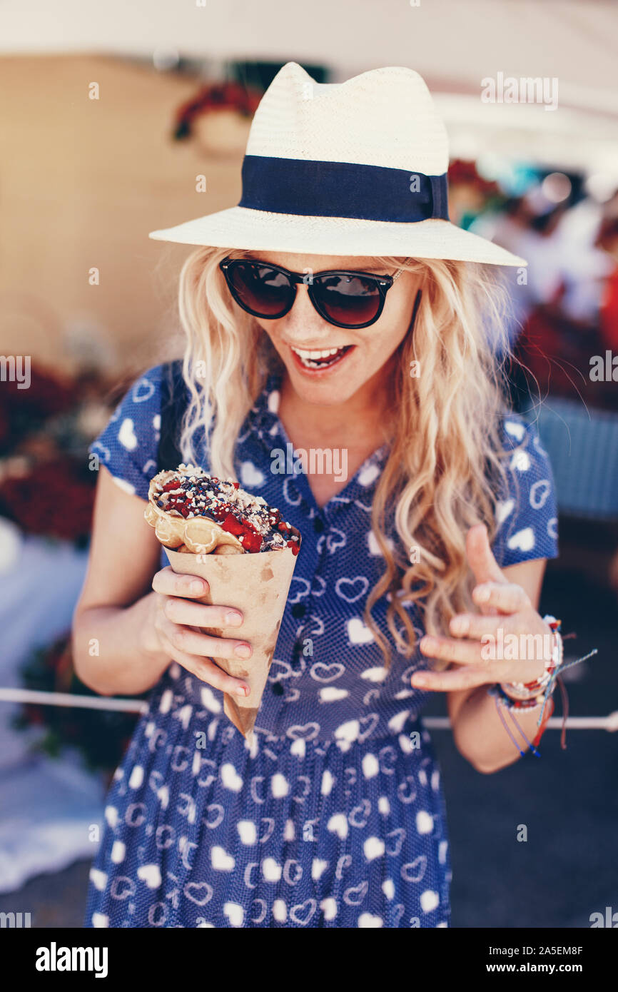 Young blonde woman in hat holding bubble waffle à Strawberry Festival Banque D'Images
