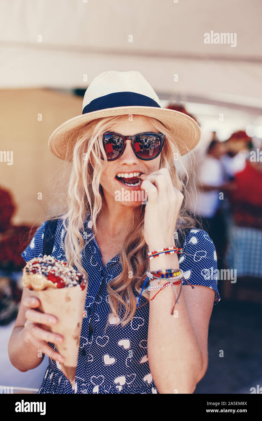 Young blonde woman in hat eating Strawberry Festival à gaufre bulle Banque D'Images