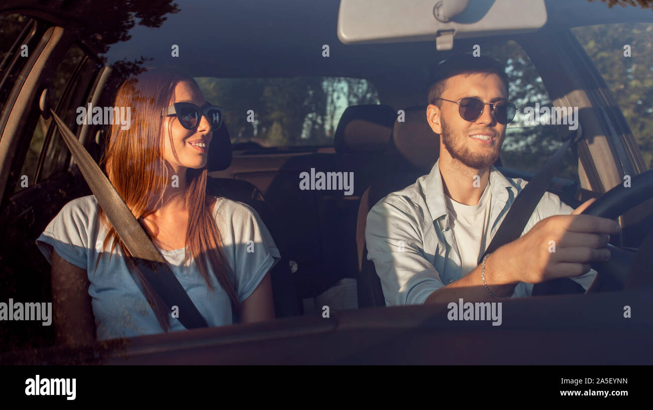 Cheerful young couple in sunglasses driving car à travers la campagne d'été à coucher du soleil Banque D'Images