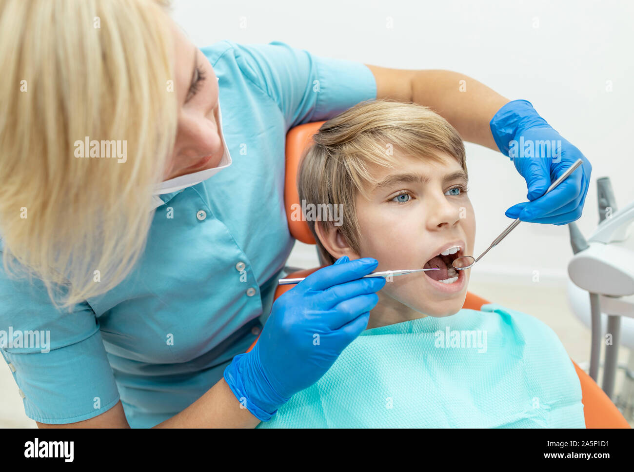 Un médecin examine attentivement le garçon les dents avec une sonde dentaire et miroir de la bouche Banque D'Images
