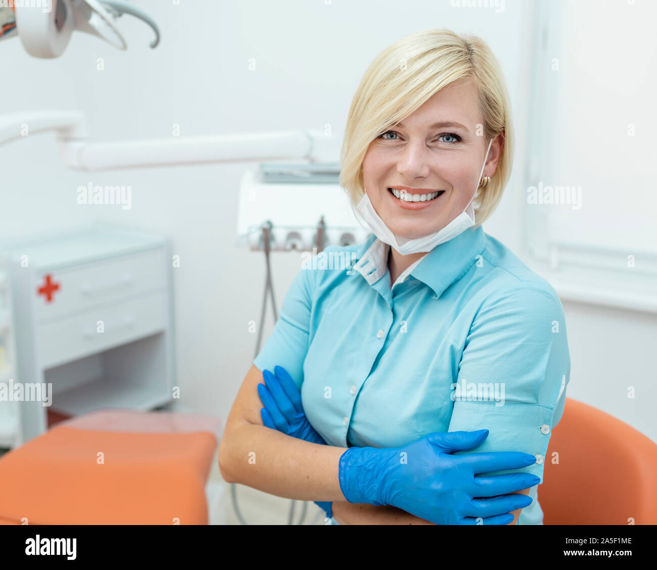 Portrait of smiling blonde dentiste en bleu, vous y trouverez des gommages corporels et des gants Banque D'Images