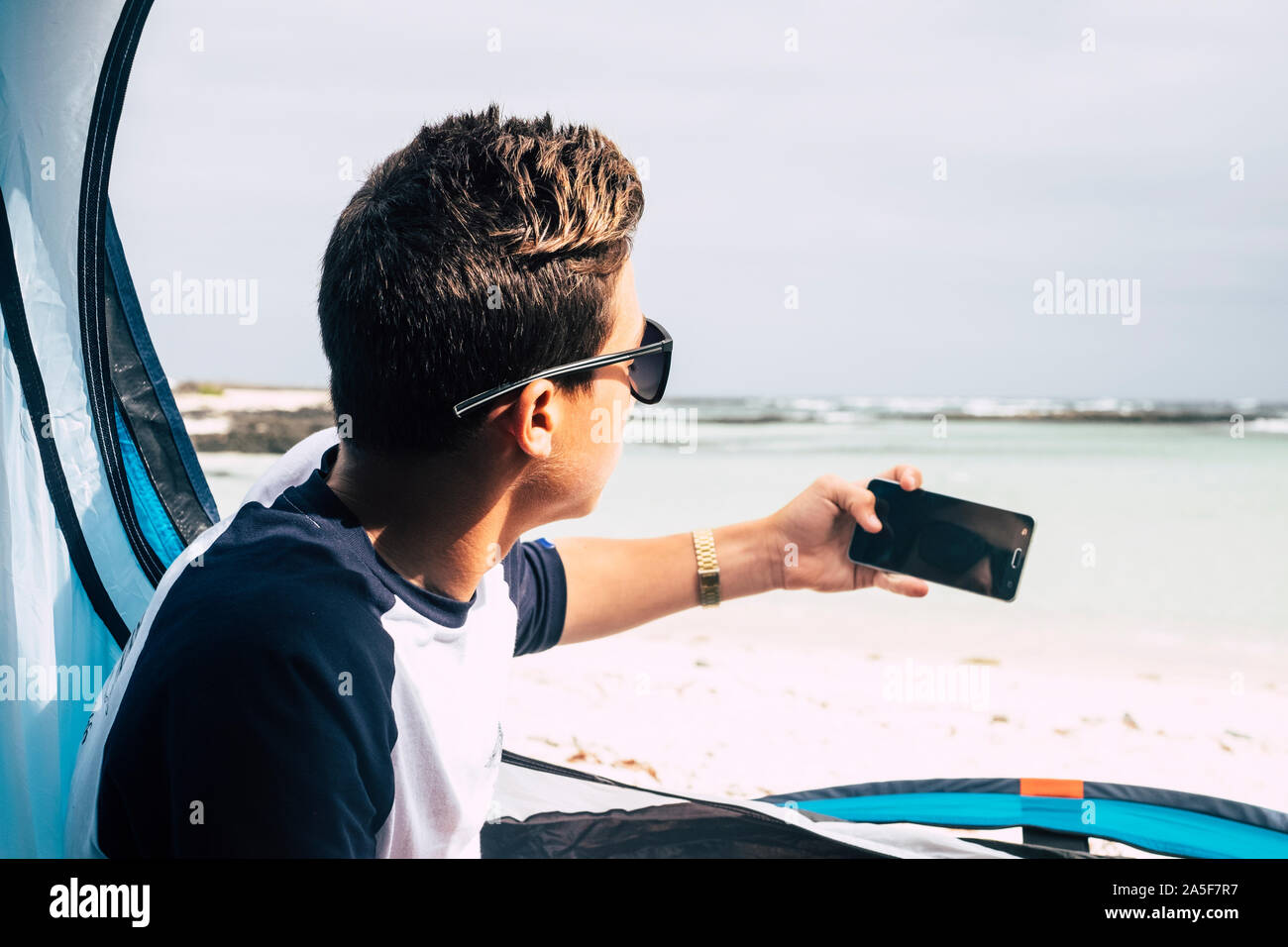 Les jeunes gens de race blanche beau garçon vu de l'arrière en tenant l'appareil photo avec la technologie moderne et de voyage - Téléphone - concept camping tropical beach Banque D'Images