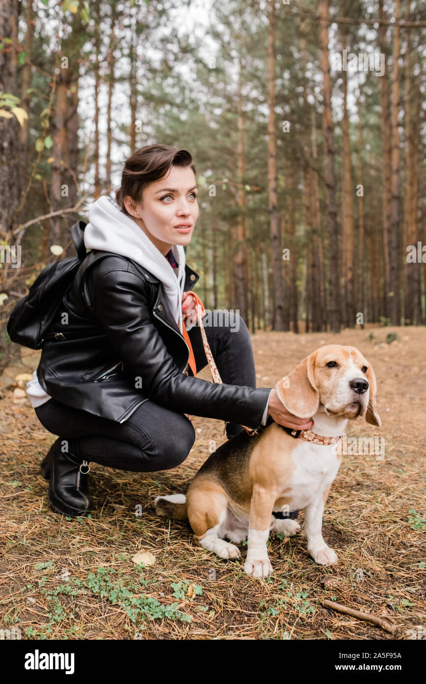 Jolie jeune femme brune caresses mignon chiot beagle, assis sur des squats durant le frisson dans l'environnement naturel Banque D'Images