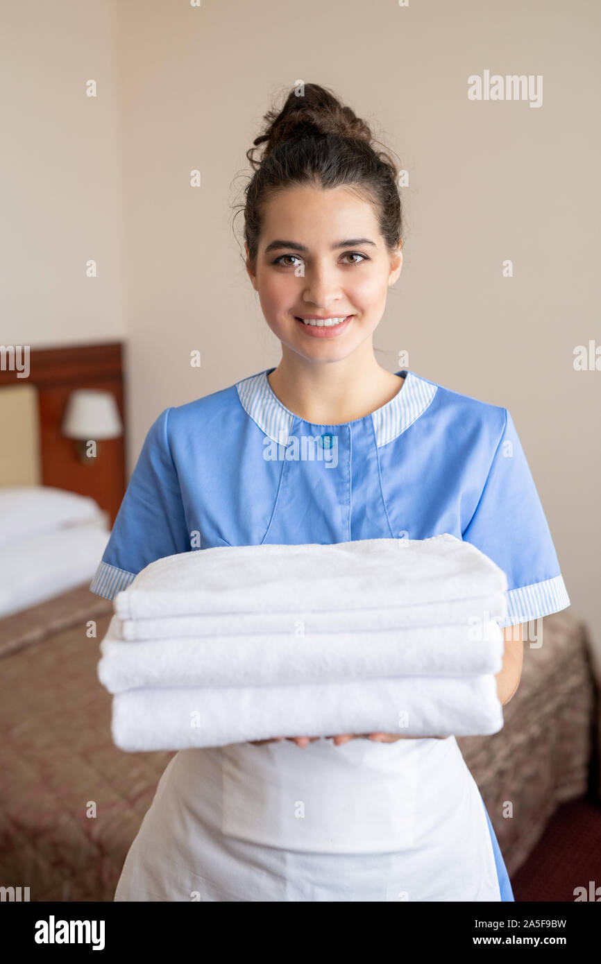 Young cheerful brunette femme de chambre avec pile de serviettes blanches clean soft standing in hotel room Banque D'Images