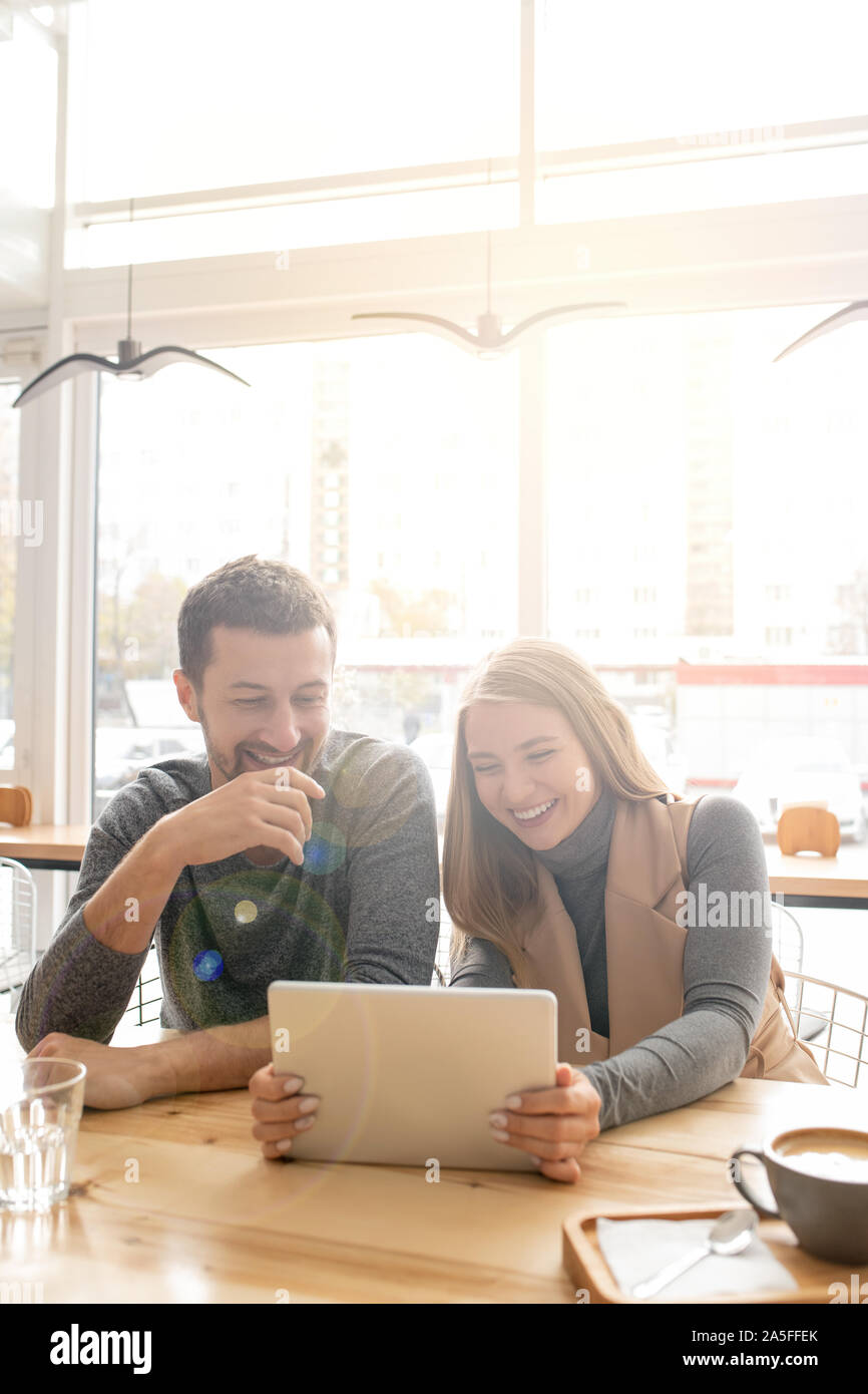 Jeune couple joyeux rire de quelque chose de drôle en regardant la vidéo en ligne en touchpad in cafe Banque D'Images