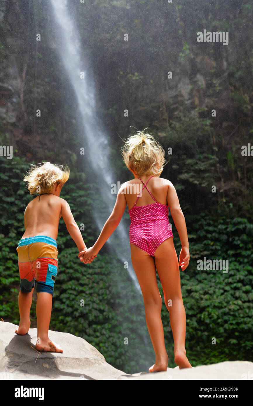 Dans la jungle tropicale heureux sœur se tenir sous une cascade, explorer la nature de la forêt tropicale. Voyage d'aventure pour les enfants, randonnée vie activité avec enfant. Banque D'Images