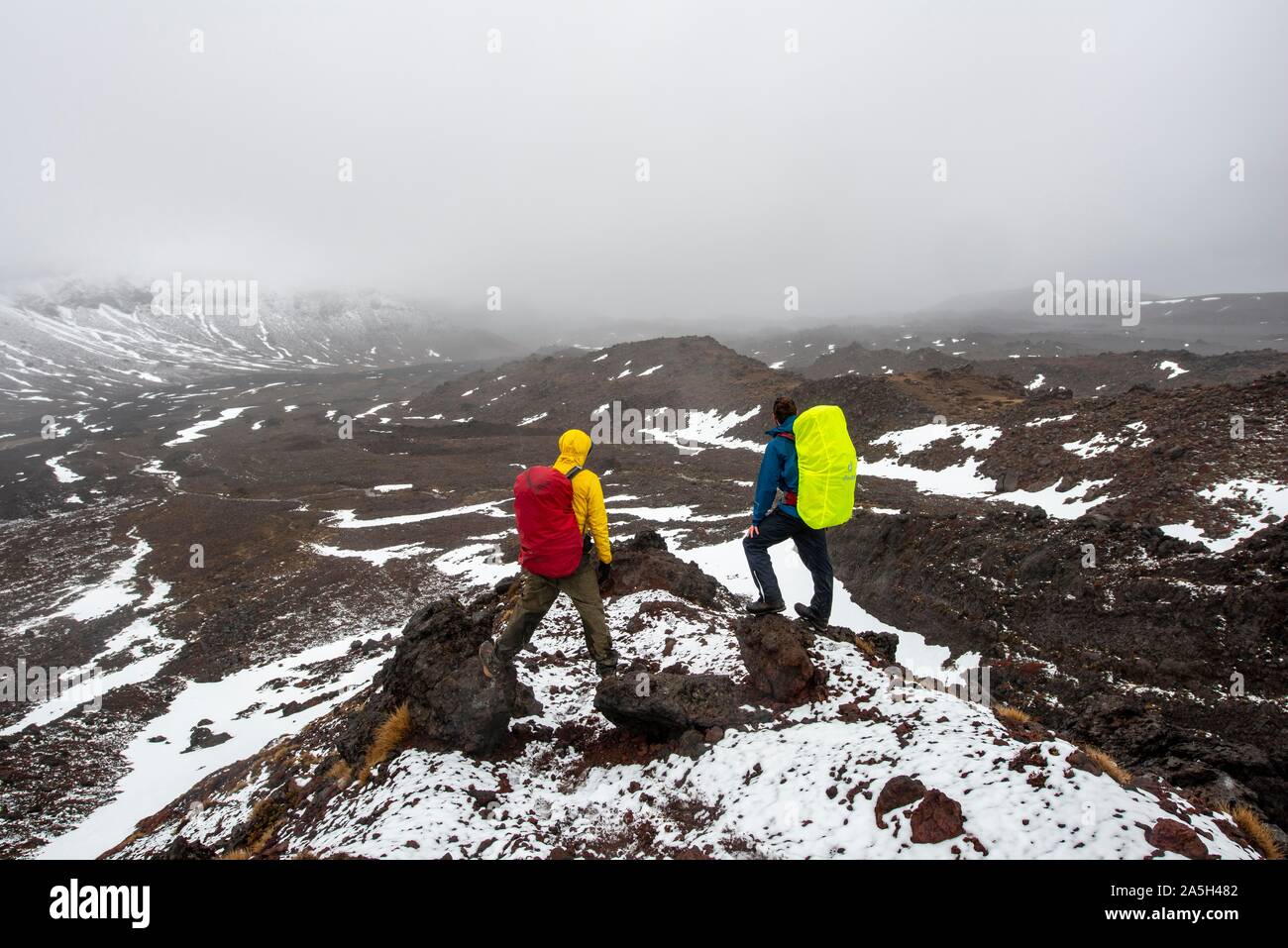 Les randonneurs debout sur des pierres, chemin de randonnée alpine Tongariro Crossing dans la neige sur des champs de lave, Parc National de Tongariro, île du Nord, Nouvelle-Zélande Banque D'Images