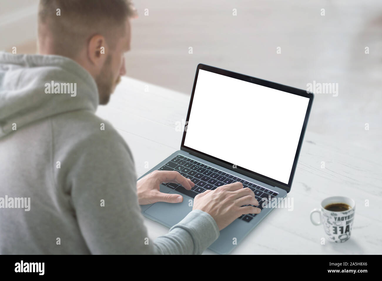Guy travailler sur ordinateur portable avec écran isolé pour une maquette. Bureau de travail propre avec tasse de café à côté. Banque D'Images