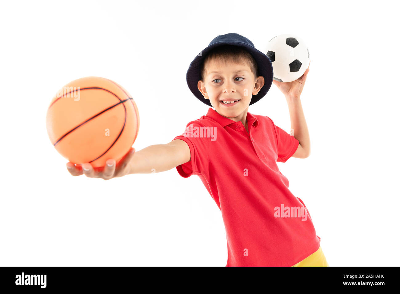 Un petit garçon au Panama, maillot jaune, short rouge et blanc sneakers les peuplements avec des ballons de foot et de basket-ball Banque D'Images