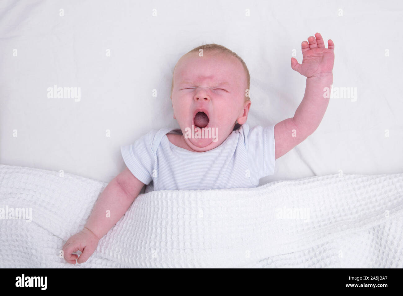 Un jeune bébé fatigué sous une couverture le bâillement Banque D'Images