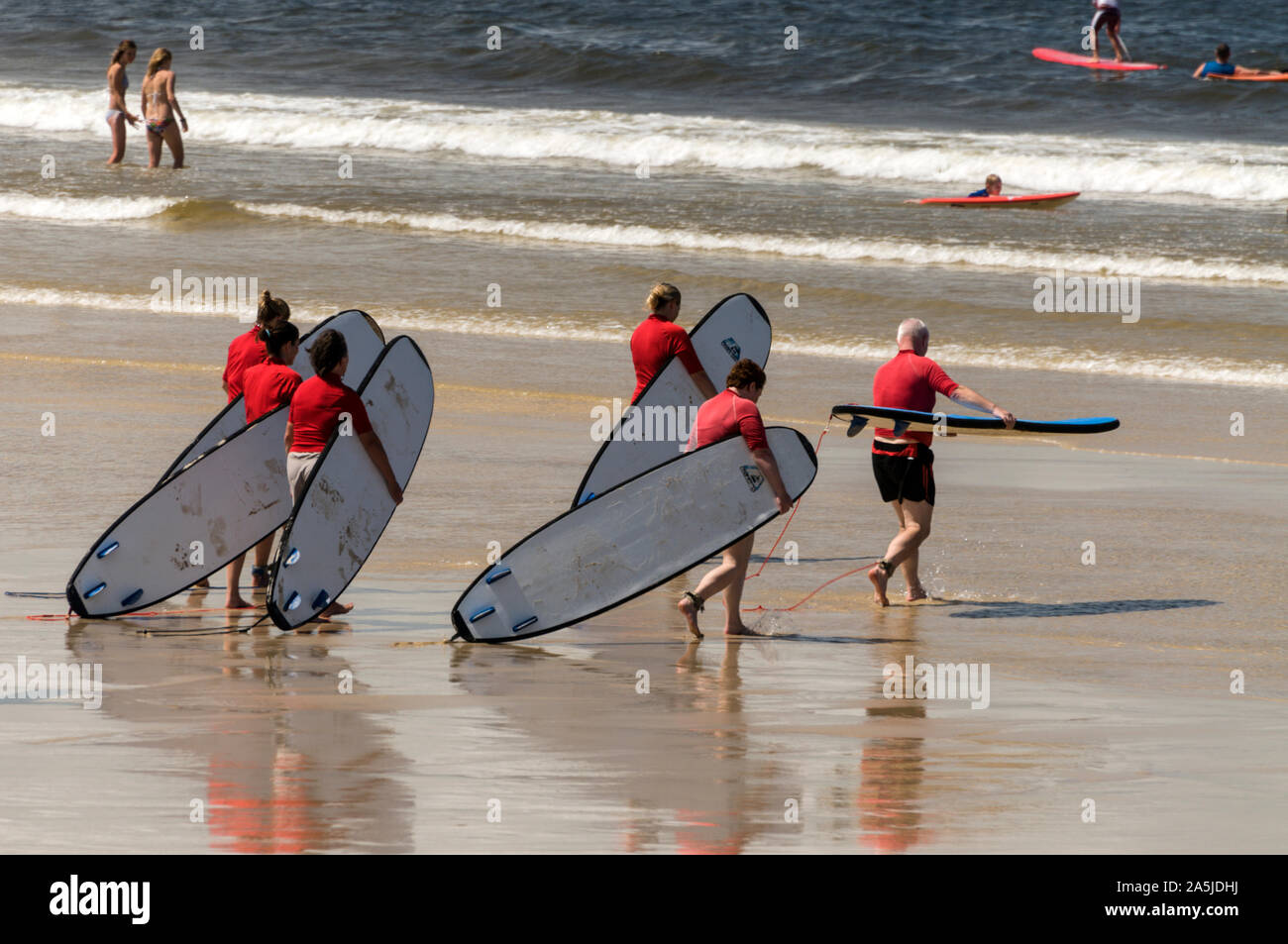 Un groupe de jeunes gens portant leurs planches de surf à la mer pour une leçon de surf à Noosa Heads sur la Sunshine Coast, Queensland, Australie Banque D'Images