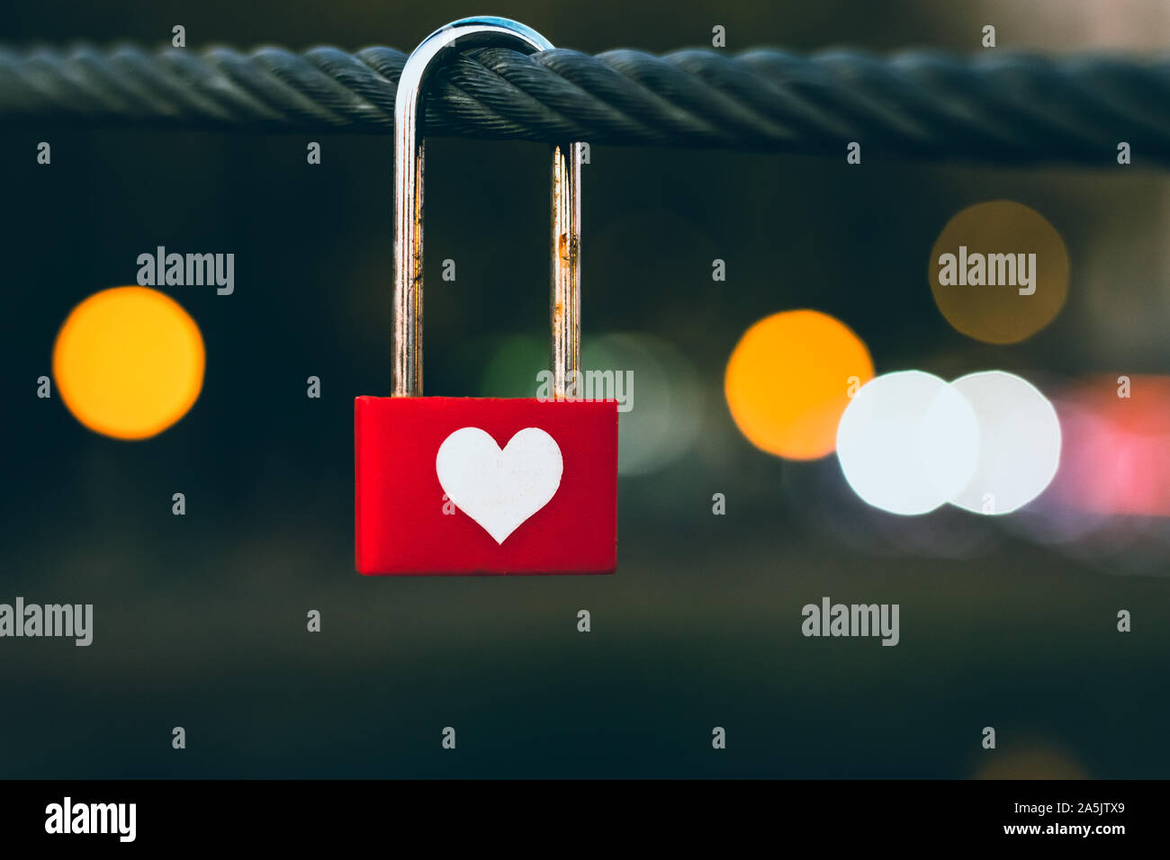 Coeur accroché sur corde à la nuit. Cadenas rouge sur une corde, les lumières de la ville le soir de bokeh. Symbole de l'amour. Concept romantique. Banque D'Images