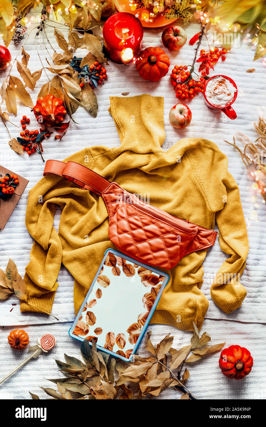 Comprimé jaune sur l'écran vide chandail tricoté avec orange taille ventre. Tasse de café avec une bougie, les citrouilles et les feuilles d'automne. Vêtements Mode d'automne. Banque D'Images