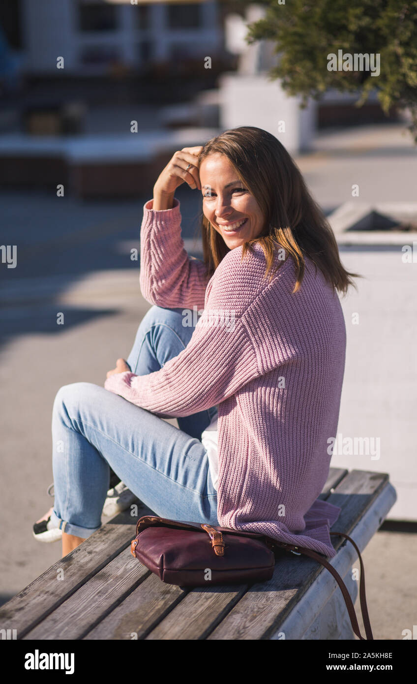 La mode la mode des jeunes filles élégantes en rose confortable chandail tricoté assis sur un banc de la ville et de rire. Banque D'Images