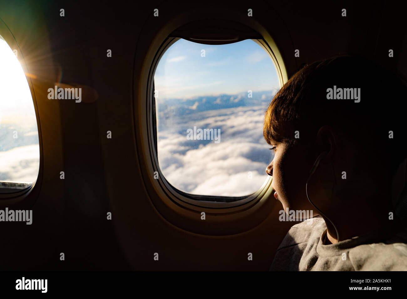 Teenage boy looking out à travers la fenêtre de l'avion à nuages sur Voyage avion Banque D'Images