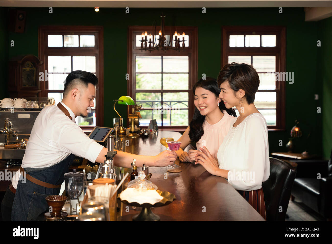 Barman qui sert des cocktails à deux jeunes femmes à bar Banque D'Images