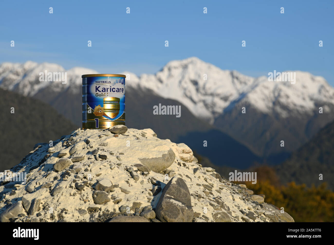 Côte ouest, la Nouvelle-Zélande, le 25 juillet 2019 : une boîte de Karicare Gold + lait pour nourrissons en poudre est assis sur une montagne de lait en poudre avec le sud des Alpes enneigées en t Banque D'Images