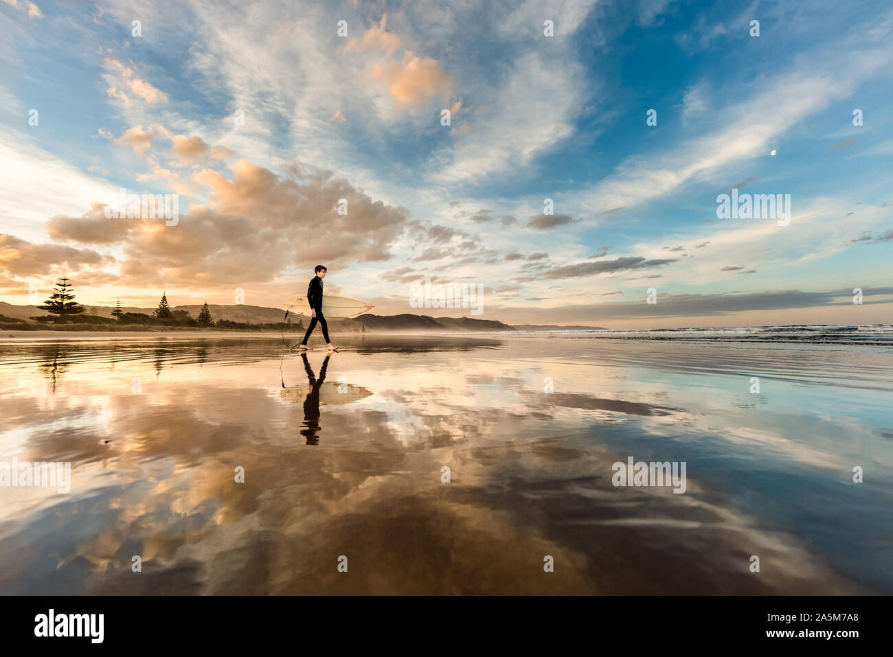 L'adolescent qui surf sur une plage en Nouvelle-Zélande au coucher du soleil Banque D'Images